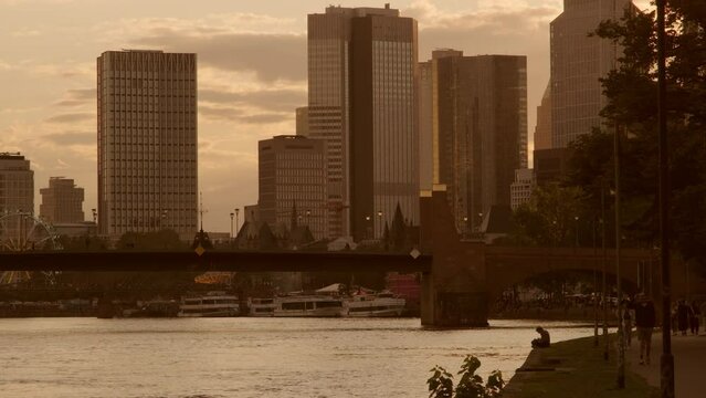Telephoto sunset silhouette of the Frankfurt Skyline framed by Ignatz Bubis Bridge. Summer evening with people walking and sitting