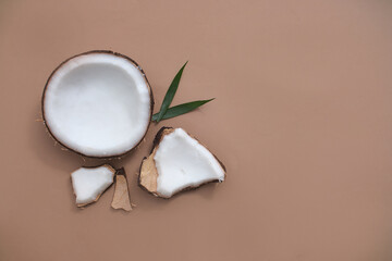 Fresh coconut and green leaves are placed next to each other. Space left for design. Coconut is a popular ingredient in food and cosmetics, it provides many nutrients for the skin and body.