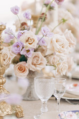 Fragment of wedding table setting, antique candlesticks, crystal, bouquets of roses in beige tones .