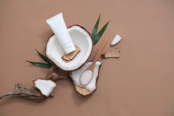 An unlabeled tube of lotion with coconut extract is placed on fresh coconut, surrounded by props. Coconut water contains a lot of lauric acid, which has the ability to reduce the aging of skin cells.