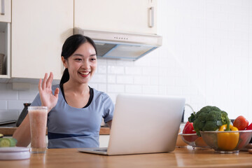 Happy woman asian in stylish tracksuit fresh smoothie shooting video with modern laptop in kitchen