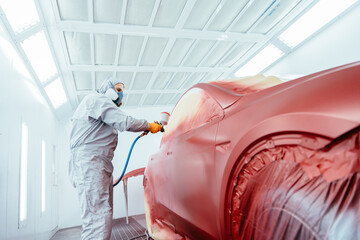 Person spray painting car in red color in special car chamber. Car service station. Worker painting...