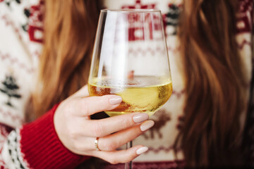 Woman drinking wine. White wine drinking. Wine glass in hand. Girl in woolen sweater alcohol. Cozy winter  background. Female hand holding wine glass. Christmas pattern season clothing. Long hair.