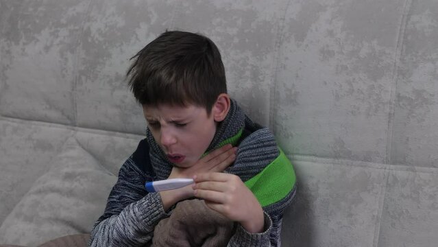 A sick student misses school. He lies under a blanket with a fever and coughs.