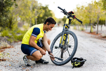 Horizontal photo of an adult with a prosthetic arm and dressed in sportswear is bent over inflating a mountain bike tire with an air pump. Disabled cyclists concept. Athletes with an amputated arm.