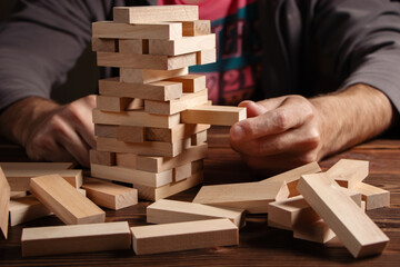 man hands making stack of wooden blocks for jenga game on dark brown table, while staying home...
