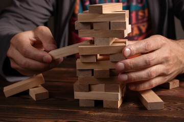 Hand of engineer playing a blocks wood tower game jenga on blueprint or architectural project