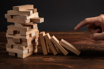 Close-up of fingers pushing a wooden Jenga block with financial risk management and strategic planning domino concepts.