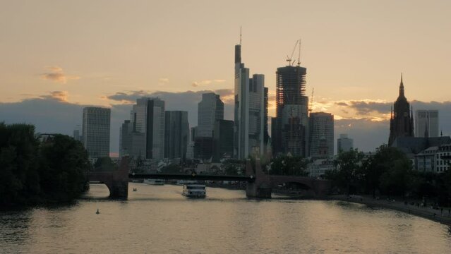 Frankfurt skyline and River Main at sunset from Ignatz Bubis Bridge. A tour boat passes under Alte Bridge