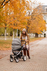 Obraz premium A young mother with a stroller walks through the autumn park. Walking with an infant in the open air in a pine forest. Newborn, family, child, parenthood.