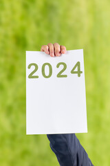 2024, Man holding cardboard with number 2024 on green background. Happy New Year