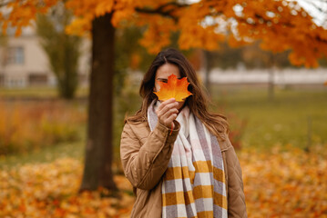 Beautiful European brunette with a autumn leave in her hands against the backdrop of an autumn park