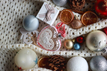 Various colorful Christmas ornaments, small presents and seasonal spices on white knitted blanket. Top view.