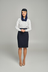 full length of happy air hostess in arabian airlines uniform standing and looking at camera on grey