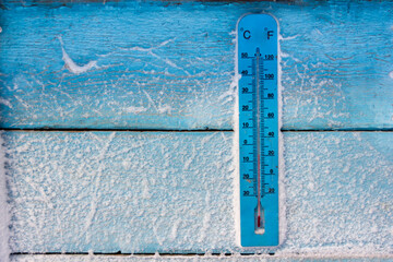 a wall of old blue boards covered with snow with a large thermometer in the frost background close-up texture