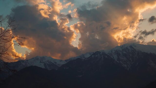 4K shot of orange clouds above the snow covered mountain peaks of the Himalayan mountain range at Manali, Himachal Pradesh, India during the winter season. Beautiful sunset above mountains in winter.