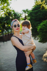 Portrait of a girl in a colored turban with red lips against a background of greenery in the park holding a child in her arms. Mother and daughter