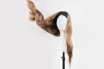 Natural looking dark blonde wig on white mannequin head. Long fair hair cut on the plastic wig...