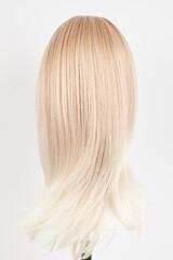 Naklejka premium Natural looking blonde wig on white mannequin head. Long hair on the plastic wig holder isolated on white background, back view.