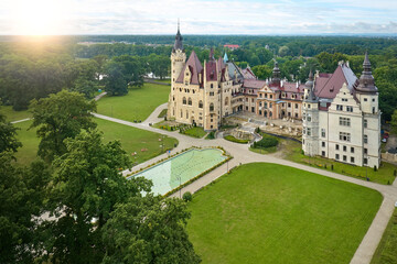 Moszna Castle from above: a fairytale castle with many towers, surrounded by a park, nicknamed the Polish Hogwarts against sunset sky.