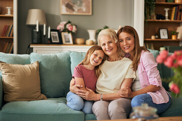 Three generations of women share a close bond, sitting cozily on a couch in a well-decorated living room. Their expressions reflect warmth, love, and the joy of being together