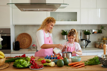 A mother and her enthusiastic young daughter engage in a bonding cooking session in their modern kitchen