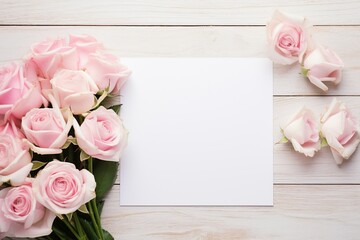 Blank white card stock on table with white and pink roses next to it, overhead view