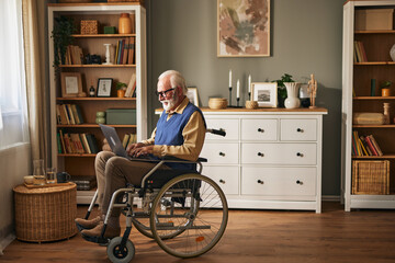 Elderly disabled man using laptop while sitting in wheelchair