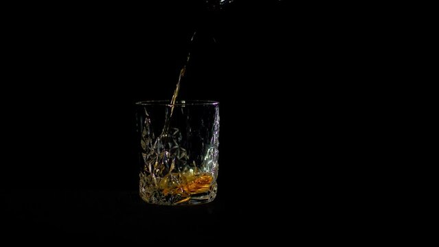 Pouring whiskey into a glass. Close-up of a vintage whiskey glass on black background. Slow motion, 4K. 
