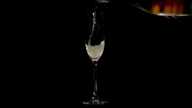 Close-up of the hand poring champagne into the glass. Charming sparkls, bubbles, foam on a black background. Slow motion, 4K 