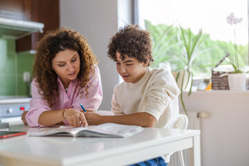 Mother helping her son with homework in kitchen at home
