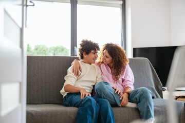 Happy mother and son sitting on sofa in living room at home 
