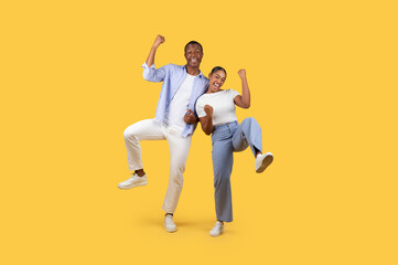 Fototapeta na wymiar Overjoyed black spouses cheering and shaking clenched fists, celebrating win, yellow studio background
