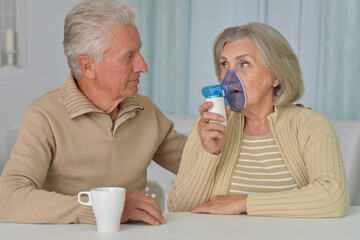 Portrait of sick senior woman with inhaler and man at home