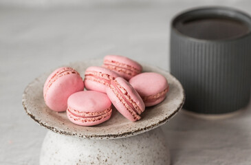 Traditional French macaroons. Pink almond cookies on a stylish ceramic plate on a gray stone background. Delicious dessert.