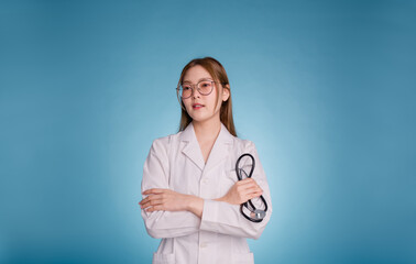 Portrait of smiling female doctor posing with arms crossed and stethoscope. Young asian doctor wear medical uniform lab coat and stethoscope isolated over blue color background. Medical staff concept.