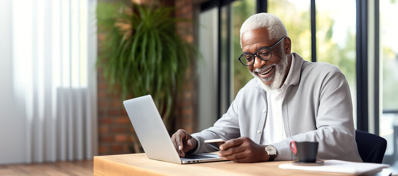 African-American elderly man typing on laptop keyboard in indoor setting, room in the background