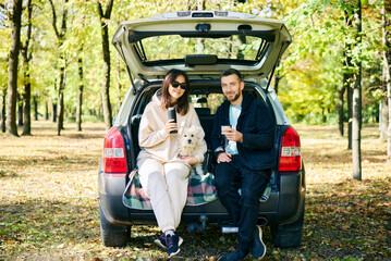 Couple with their dog relaxing in forest sitting in car trunk - obrazy, fototapety, plakaty