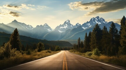 An open road leads to the Grand Teton's mountain range, rising in the distance beyond a thick pine forest. The last rays of sunlight shine on the mountain. Photo shot vertically to include more road. - obrazy, fototapety, plakaty