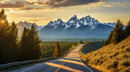 Keuken foto achterwand Tetongebergte An open road leads to the Grand Teton's mountain range, rising in the distance beyond a thick pine forest. The last rays of sunlight shine on the mountain. Photo shot vertically to include more road.