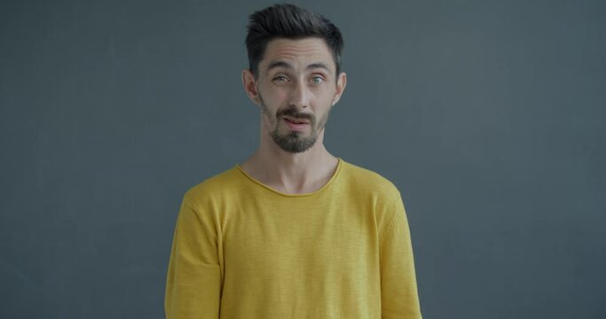 Slow motion portrait of strict young man stretching arm to camera and wagging finger forbidding standing on grey color background. People and body language concept.