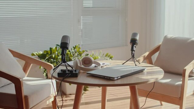 Medium long shot of round table with laptop, microphones, headphones and audio equipment prepared for recording podcast in studio