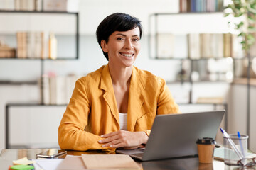 Middle aged business woman at desk posing with laptop indoor