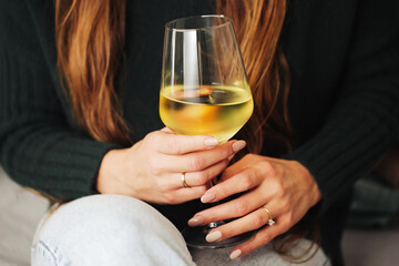 Woman drinking wine. White wine drinking. Wine glass in hand. Girl in woolen sweater. Cozy winter alcohol background. Female hand holding wine glass. Winter season clothing. Long hair shallow depth.