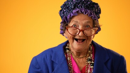 Closeup of funny happy smiling laughing crazy grandmother elderly woman, 80s, 90s, wearing cat eye glasses and hat isolated on yellow background in studio