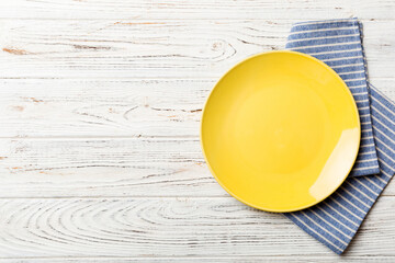 Top view on colored background empty round yellow plate on tablecloth for food. Empty dish on napkin with space for your design - obrazy, fototapety, plakaty