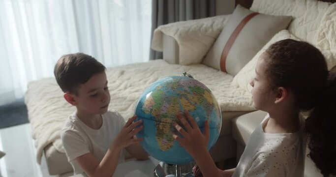 Top view children is studying while sitting at home in rays sunset in room. Kids in morning light sunset with Globe, Cute boy and little girl, technology for school boy, child looks at globe. 4K