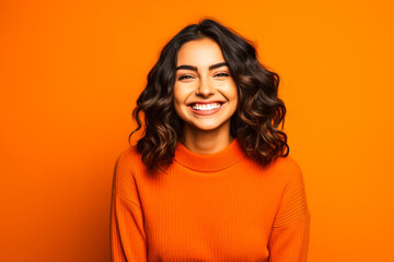 Jeune femme souriante posant avec un pull orange sur fond orange - obrazy, fototapety, plakaty