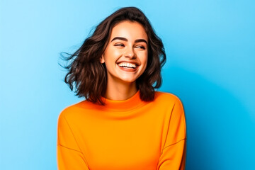 Jeune femme souriante posant avec un pull orange sur fond bleu - obrazy, fototapety, plakaty