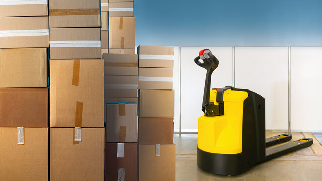 Electric pallet jack. Cardboard boxes on warehouse floor. Modern pallet jack. Equipment for warehouse work. Trolley for transporting goods. Electric pallet jack near boxes. Equipment for storehouse